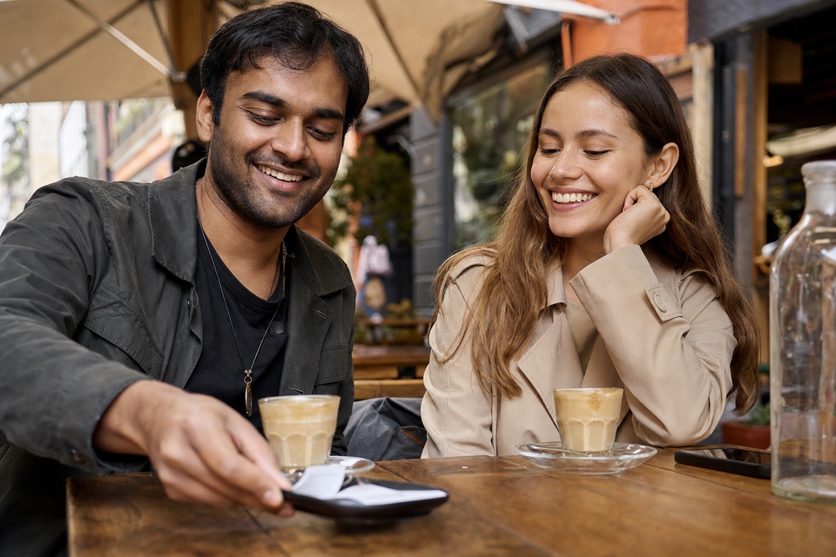 A café table with two cortados, a South Asian man and a Colombian woman, one reaching to pick up the bill