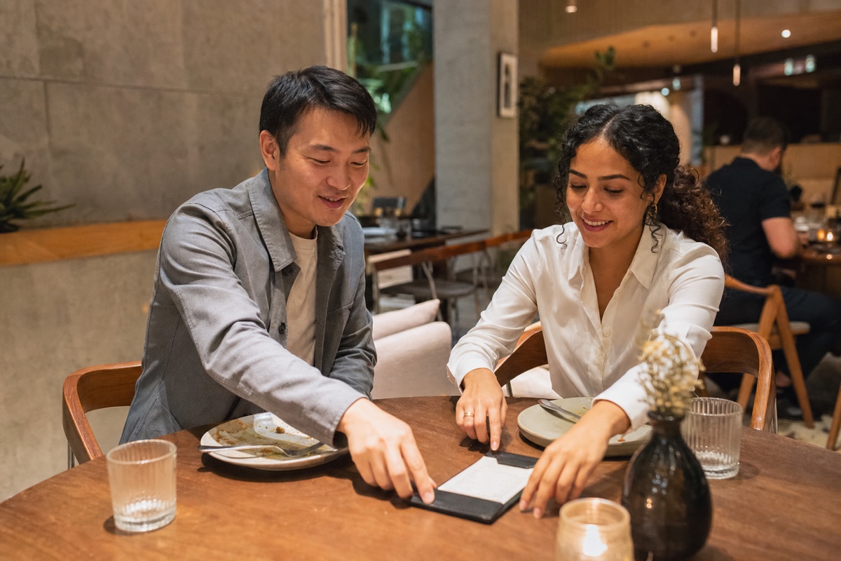 A Mexican woman and a foreign man discussing the bill after a relaxed dinner, with both reaching toward it without tension